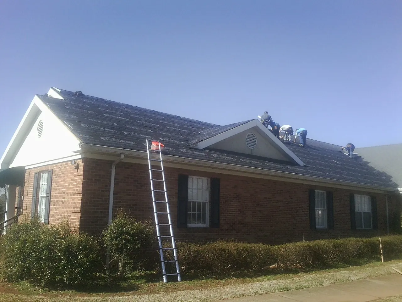 Crew tearing shingles off a brick ranch roof with a ladder set — Metal Roof Repair work by our crew in Rochelle Park