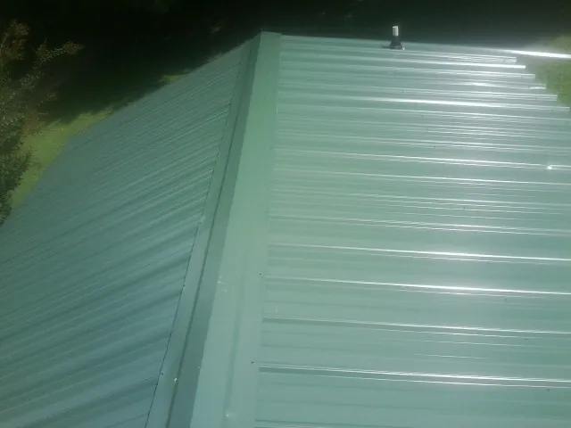New green metal panels meeting at the ridge of a roof — Flat Roof Repair work by our crew in Rochelle Park