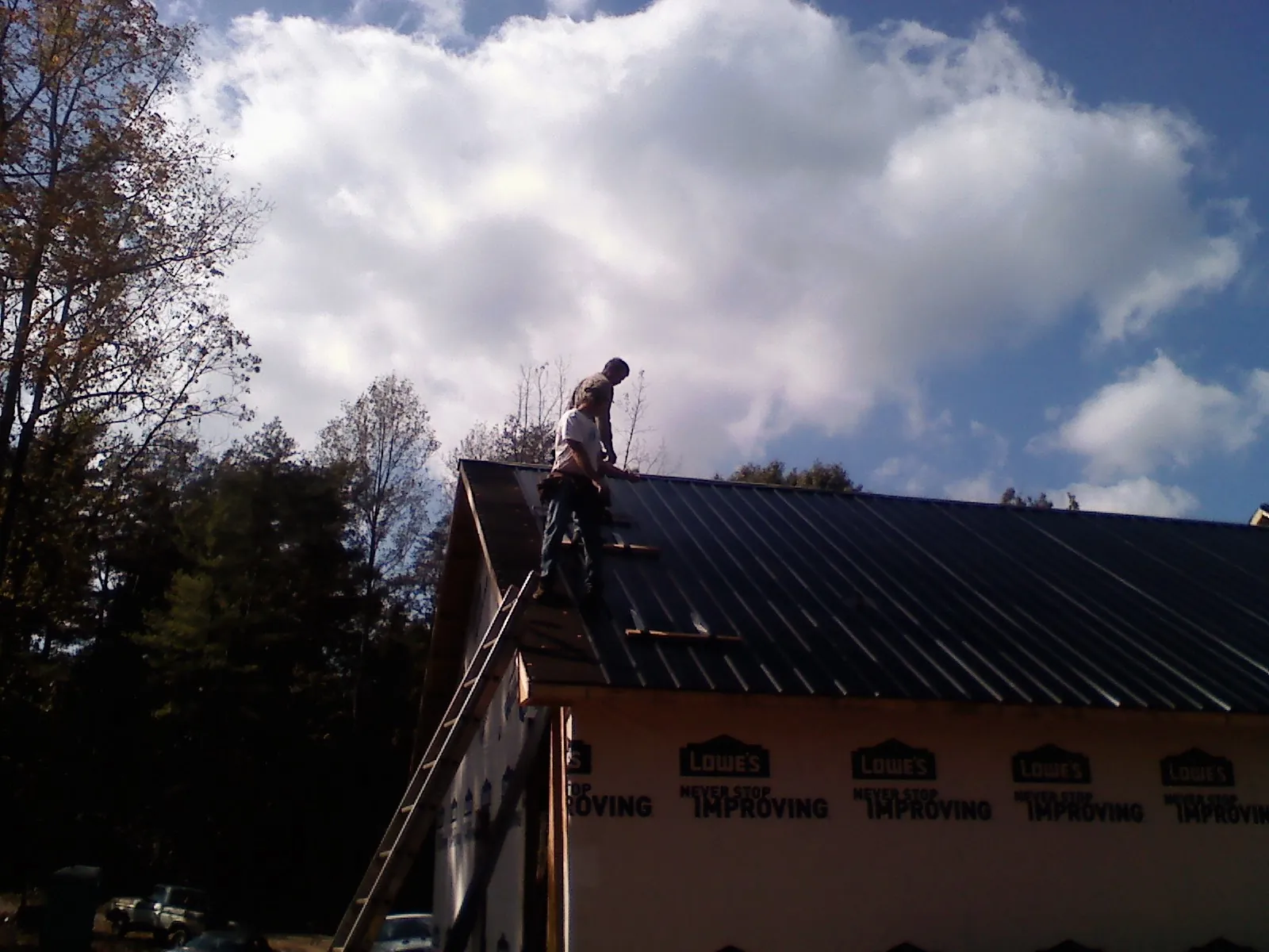 Roofer fastening dark metal panels high against a cloudy sky, from a Roof Inspection job in Rochelle Park
