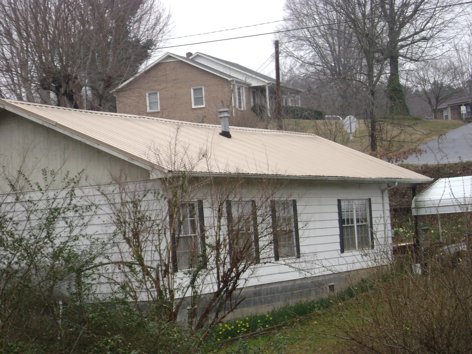 Tan metal roof on a white sided house set into a hillside — Commercial Roofing by Roofing Brothers in Rochelle Park